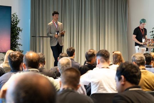 Sami on stage with microphone, checking the next session